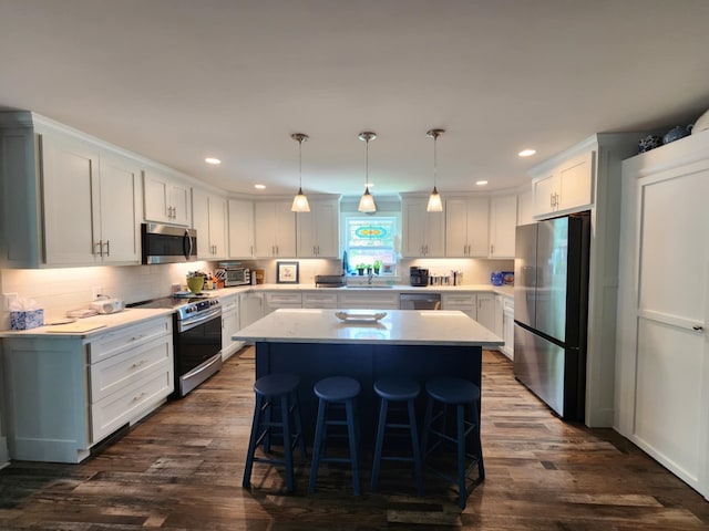 kitchen with stainless steel appliances, a kitchen island, dark wood-type flooring, a sink, and a kitchen bar