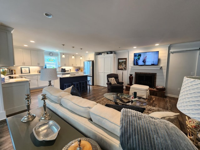 living area with dark wood-style flooring, a large fireplace, and recessed lighting