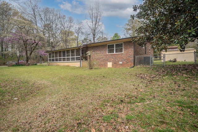 rear view of house with a gate, fence, brick siding, a sunroom, and a lawn