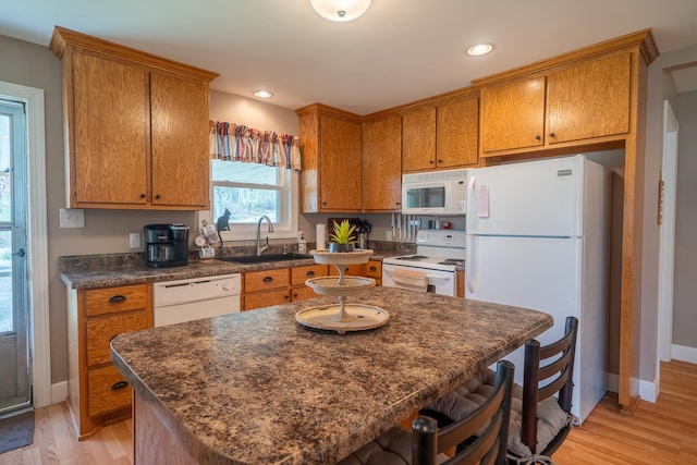 kitchen featuring light wood-style flooring, white appliances, brown cabinets, dark countertops, and a sink