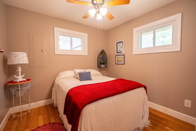 bedroom with a ceiling fan, electric panel, baseboards, and wood finished floors