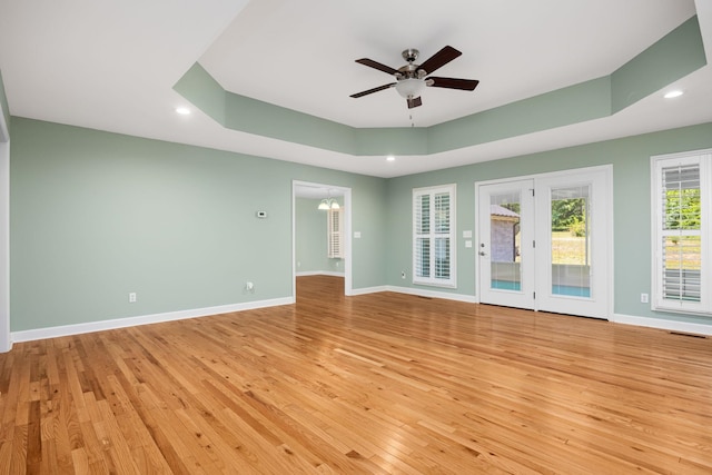 spare room with light wood finished floors, baseboards, a tray ceiling, and ceiling fan