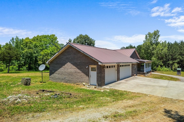 view of side of property with metal roof, an attached garage, brick siding, concrete driveway, and a lawn