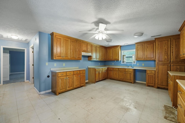 kitchen featuring under cabinet range hood, a ceiling fan, light countertops, brown cabinets, and light floors