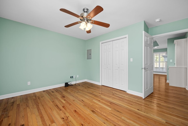 unfurnished bedroom featuring ceiling fan, baseboards, a closet, electric panel, and light wood finished floors