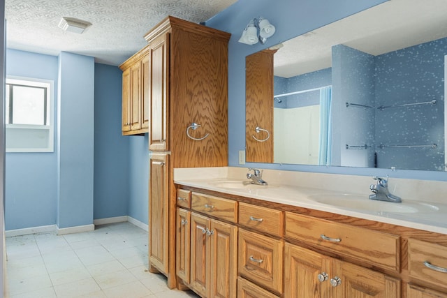 bathroom with a textured ceiling, double vanity, a sink, and baseboards