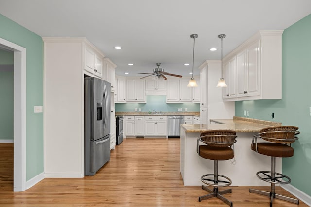 kitchen with a peninsula, white cabinets, appliances with stainless steel finishes, light wood-type flooring, and a kitchen bar