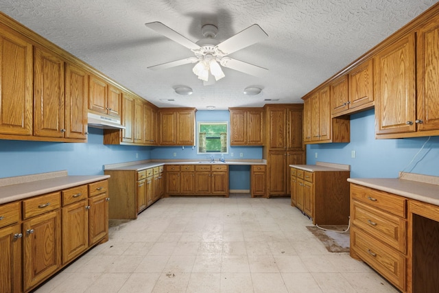 kitchen featuring under cabinet range hood, built in desk, a sink, and brown cabinets