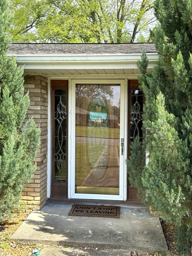  - view of exterior entry with brick siding and roof with shingles