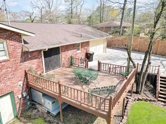 wooden terrace featuring fence, an attached garage, outdoor dining space, stairway, and driveway