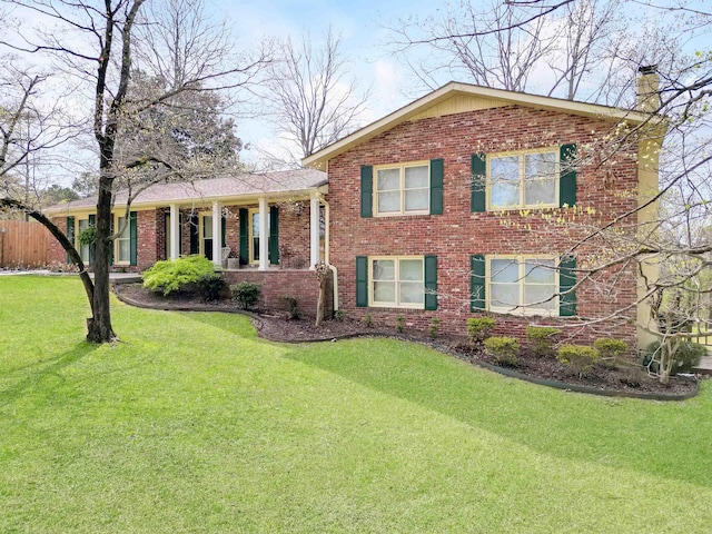tri-level home featuring a chimney, brick siding, fence, and a front lawn