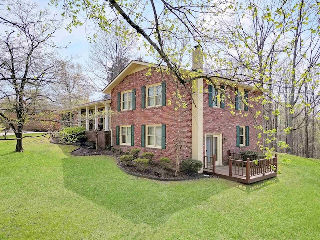 exterior space with a lawn, brick siding, a chimney, and a deck