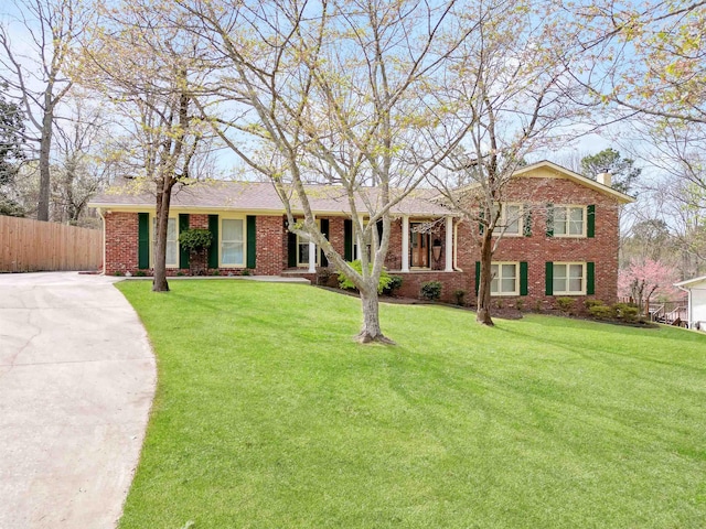 view of front of property with brick siding, driveway, fence, and a front lawn