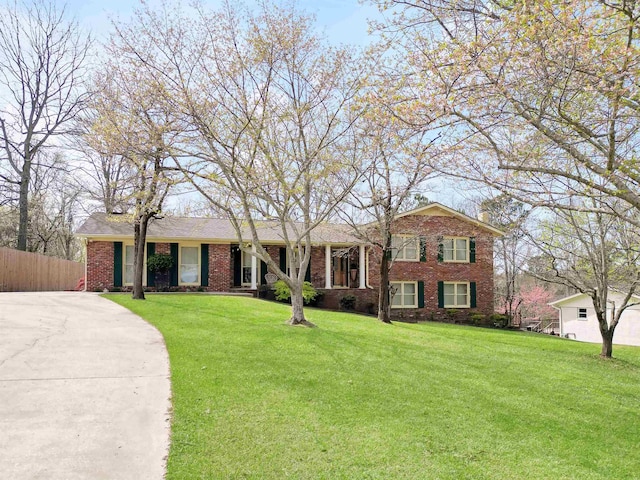 view of front of home with brick siding, driveway, fence, and a front lawn