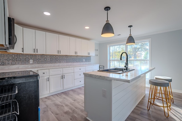 kitchen with a center island with sink, a kitchen breakfast bar, sink, hanging light fixtures, and white cabinetry