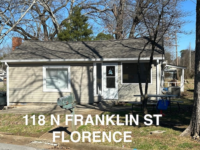 view of front of house featuring entry steps, a chimney, and roof with shingles