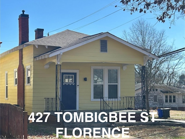 view of front of home with a porch, roof with shingles, a chimney, and fence