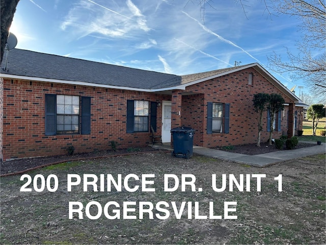 view of front of property featuring uncovered parking, brick siding, and roof with shingles