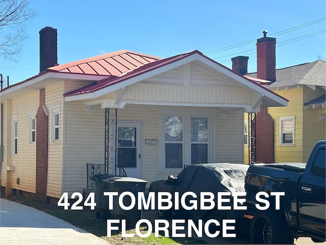 bungalow-style house featuring covered porch, metal roof, and a chimney