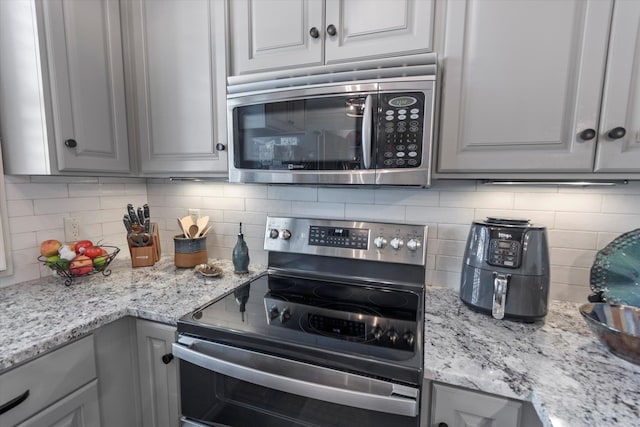  - kitchen with stainless steel appliances, gray cabinetry, backsplash, and light stone countertops