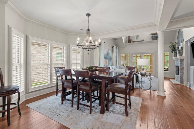  - dining area featuring a chandelier, ornate columns, wood finished floors, a stone fireplace, and crown molding