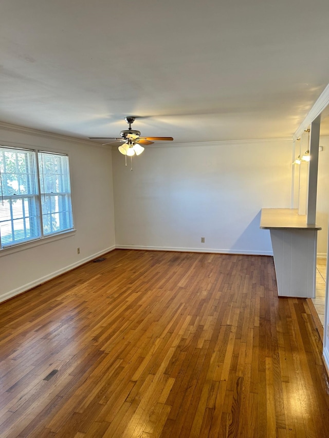 spare room with ceiling fan, visible vents, baseboards, ornamental molding, and hardwood / wood-style floors