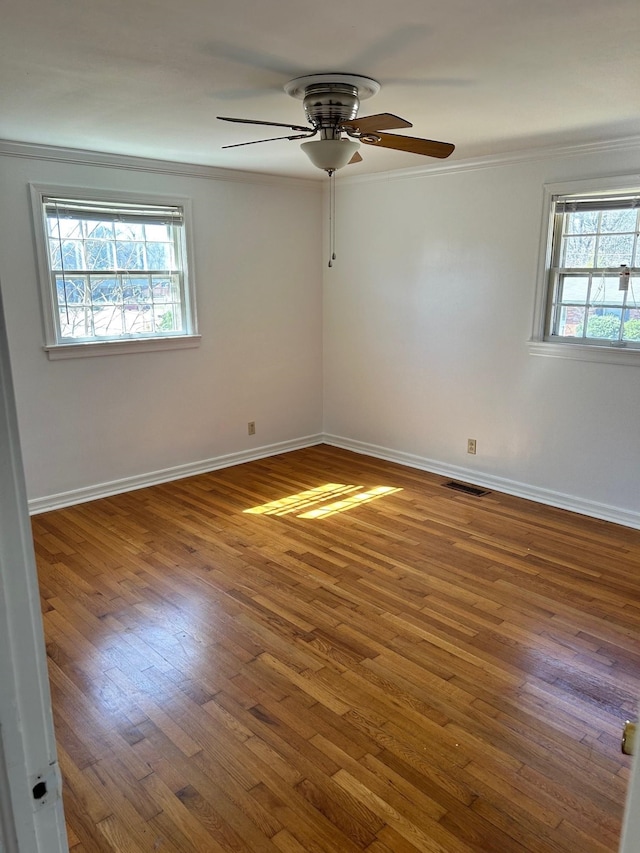 empty room featuring ornamental molding, visible vents, plenty of natural light, and wood finished floors