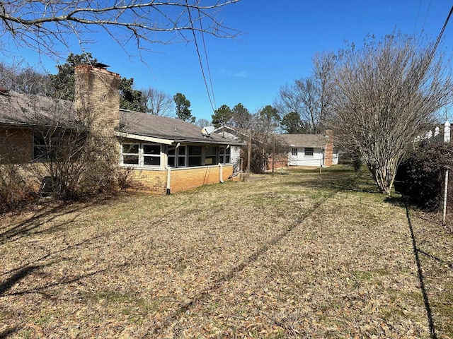 rear view of house with a sunroom, a chimney, brick siding, and a yard