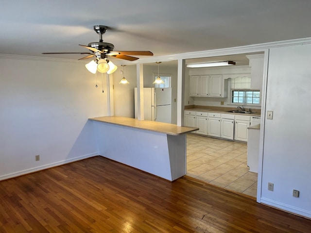 kitchen with freestanding refrigerator, a peninsula, light wood-type flooring, white cabinetry, and a sink