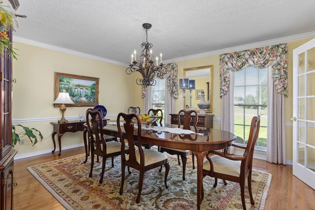 dining room with a textured ceiling, ornamental molding, a notable chandelier, and light wood-type flooring