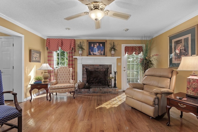 living area featuring ornamental molding, a textured ceiling, ceiling fan, hardwood / wood-style flooring, and a fireplace