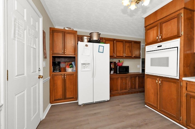 kitchen with light wood-type flooring, ornamental molding, a textured ceiling, white appliances, and a chandelier