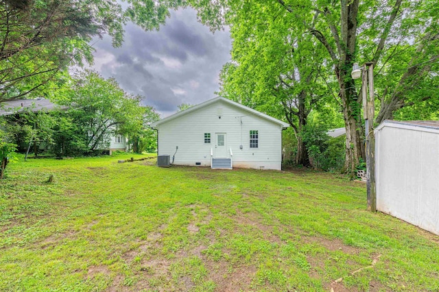 rear view of house featuring crawl space, central AC, a yard, and an outbuilding
