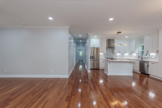 kitchen with appliances with stainless steel finishes, wall chimney range hood, tasteful backsplash, white cabinetry, and ornamental molding