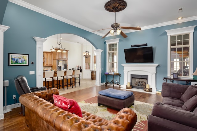 living room with wood-type flooring, ceiling fan with notable chandelier, and ornamental molding