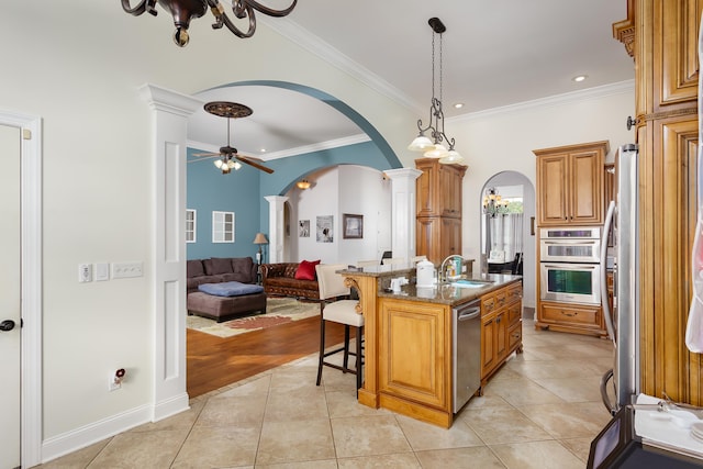 kitchen with stone counters, a center island with sink, a kitchen breakfast bar, light tile patterned floors, and ornate columns