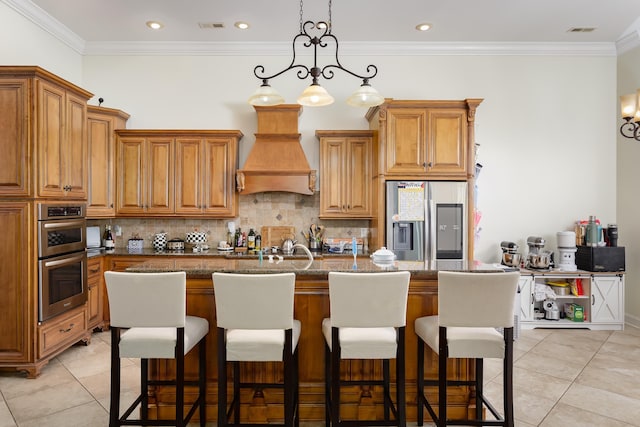 kitchen with stainless steel appliances, pendant lighting, a center island with sink, light tile patterned floors, and custom range hood