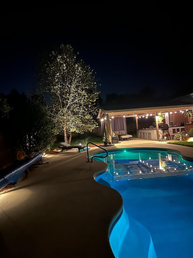 pool at night featuring a patio area