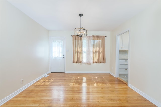 unfurnished dining area with a chandelier, light wood-style floors, and baseboards