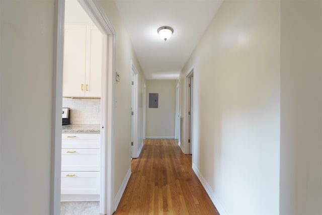 corridor with light wood finished floors, electric panel, and baseboards