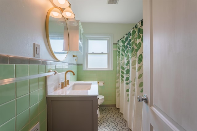 bathroom featuring tile walls, toilet, vanity, a wainscoted wall, and tile patterned floors