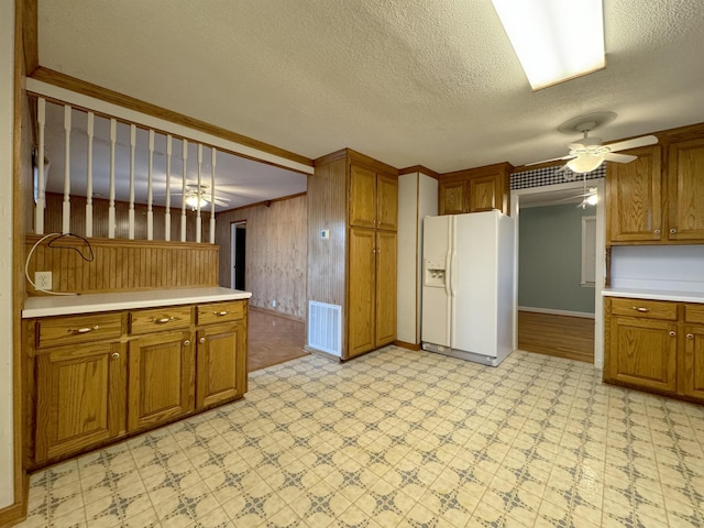 kitchen featuring a textured ceiling, ceiling fan, wooden walls, white refrigerator with ice dispenser, and pendant lighting