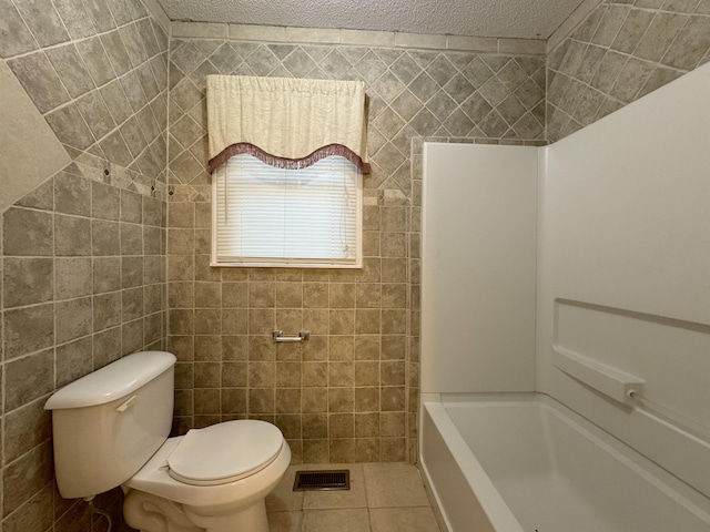 bathroom with tile patterned flooring, a textured ceiling, toilet, and tile walls