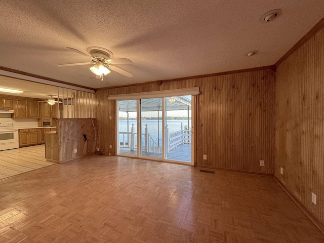 unfurnished living room with wooden walls, light parquet floors, a water view, and ceiling fan