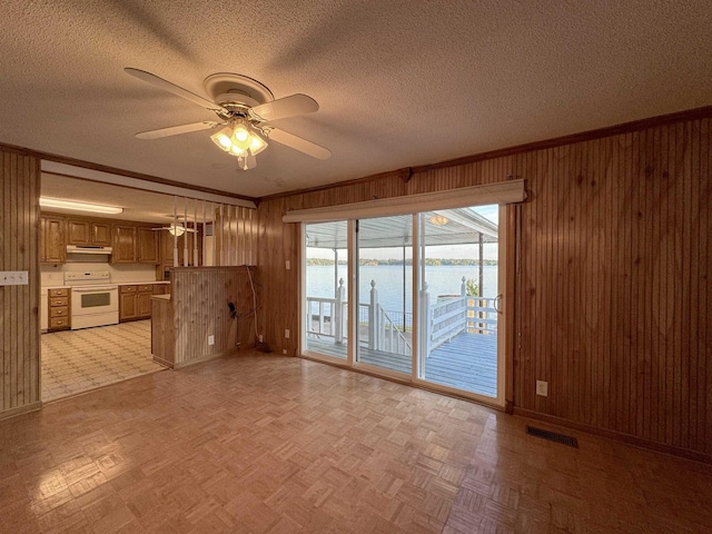 unfurnished living room with light parquet flooring, a water view, ceiling fan, and wood walls