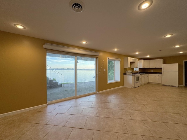 kitchen featuring white cabinets, light tile patterned floors, white appliances, and a water view