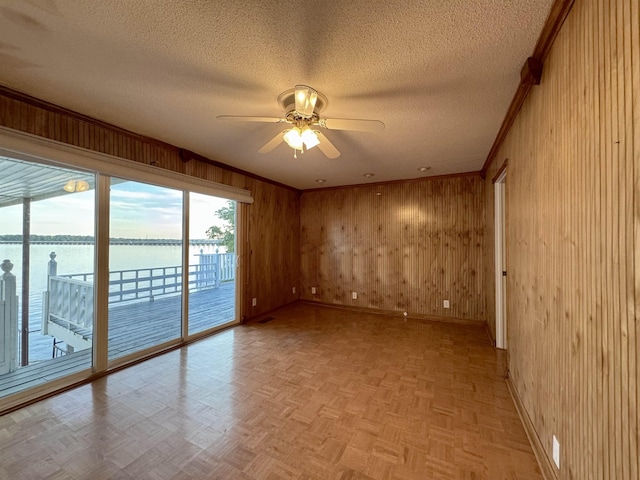 unfurnished room featuring ceiling fan, wood walls, a water view, and light parquet flooring