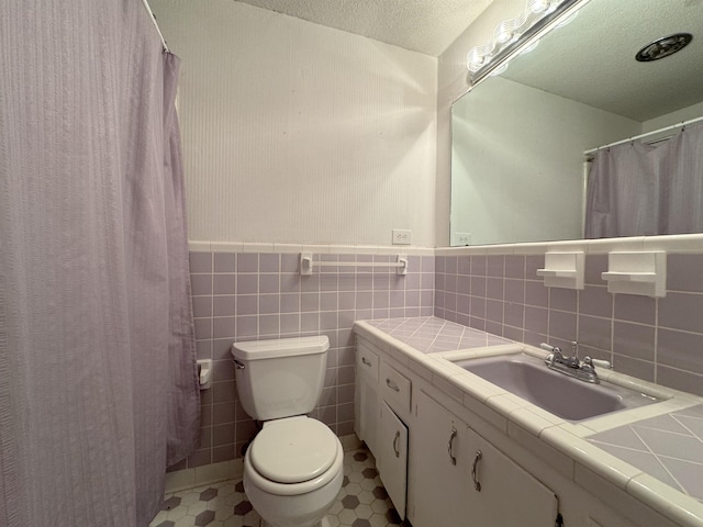 bathroom with vanity, a shower with curtain, toilet, a textured ceiling, and tile walls