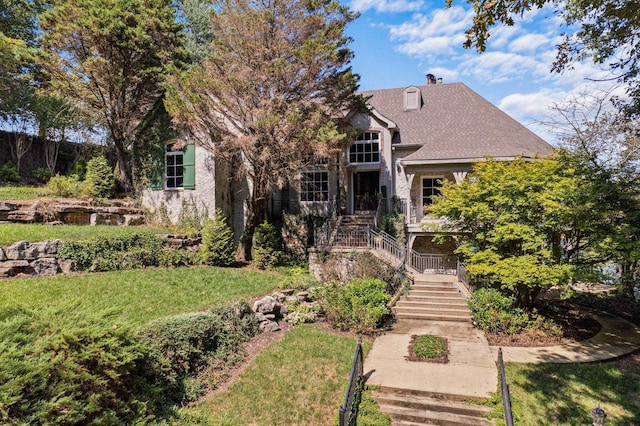  - view of property hidden behind natural elements featuring a front yard, a chimney, and stairs