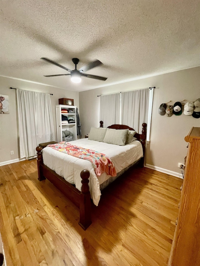 bedroom with wood finished floors, baseboards, a textured ceiling, and a ceiling fan